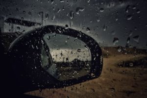 Close-up of a car side mirror with raindrops, capturing a wet and stormy atmosphere.